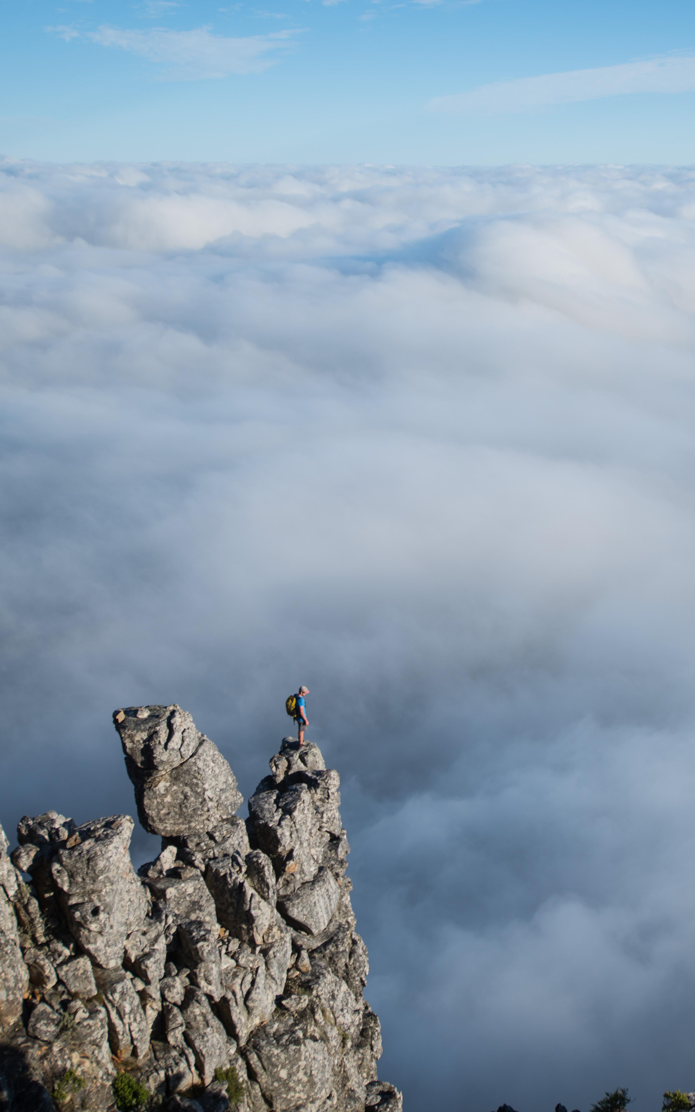 Man stands on the edge of a high mountain surrounded by clouds