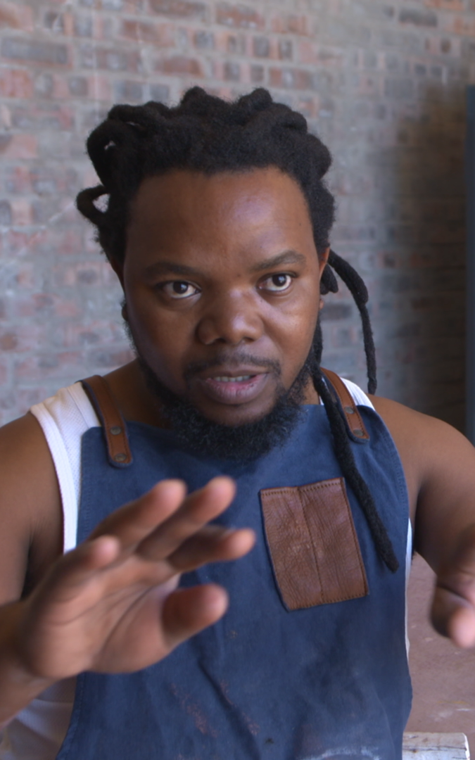 Black ceramicist sitting by his workbench.