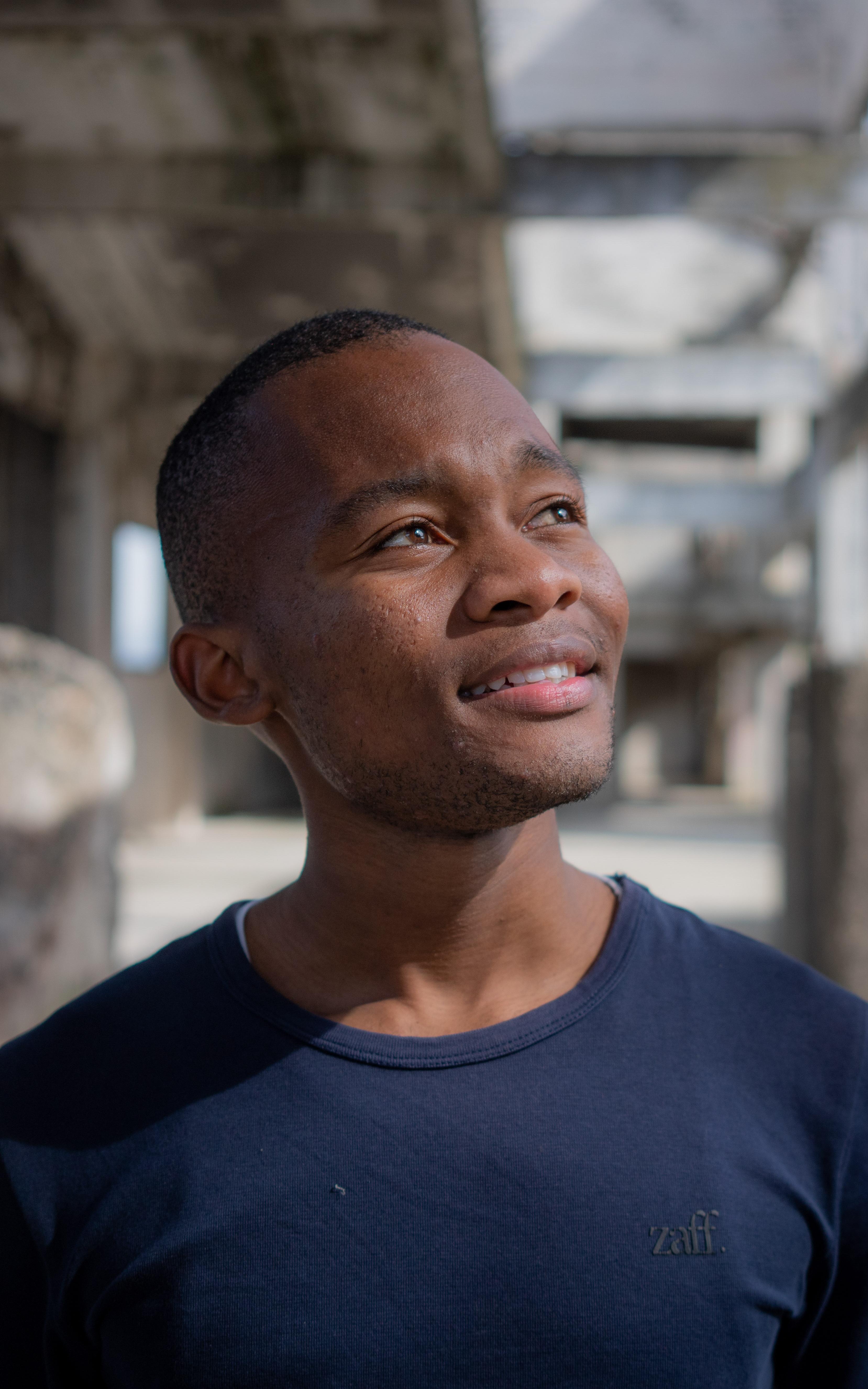 Beautiful News - Aphiwe Koti of Street Dogs Documentary standing thoughtfully with building ruins in background.