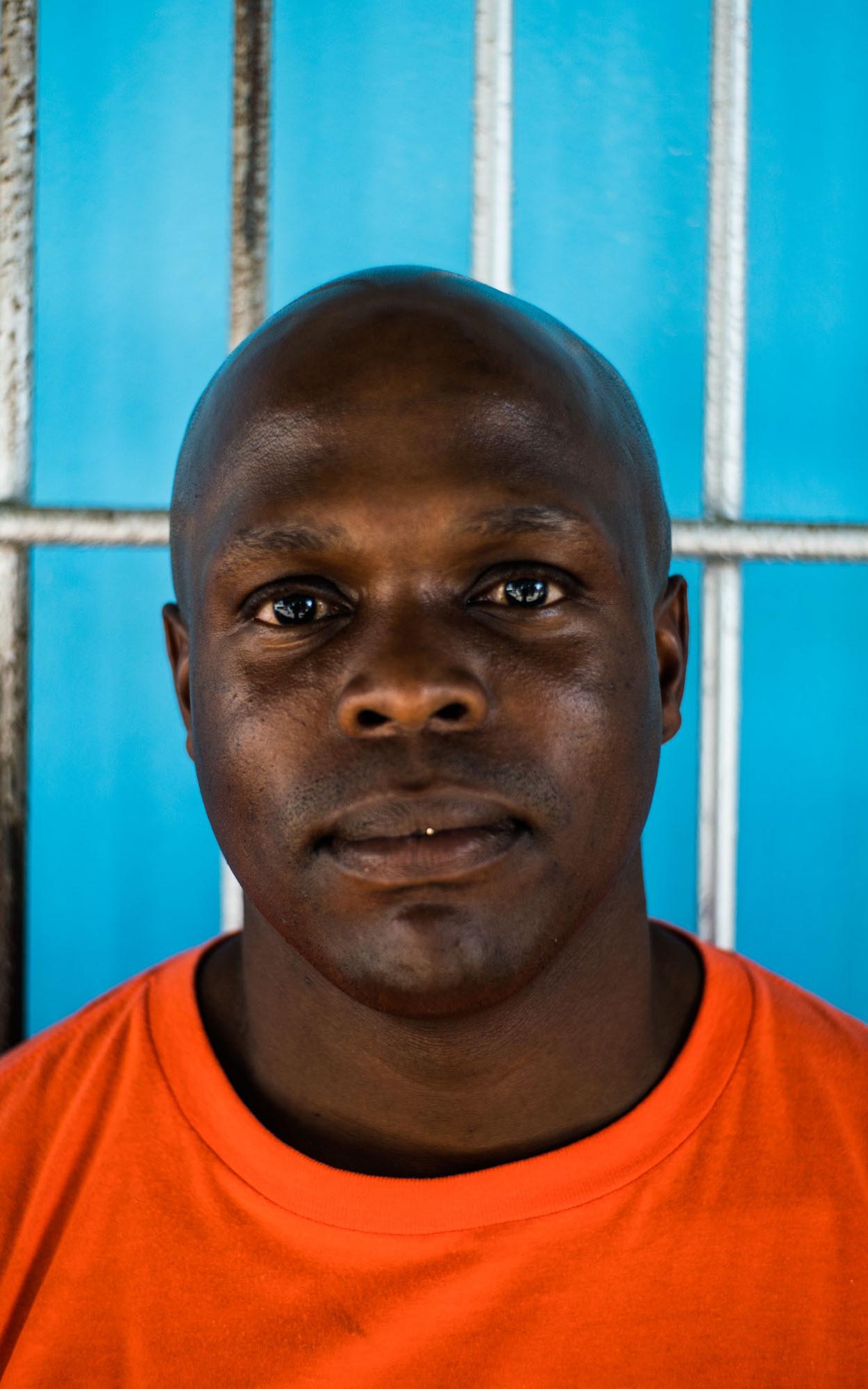 Black man staring into camera in front of blue wall.