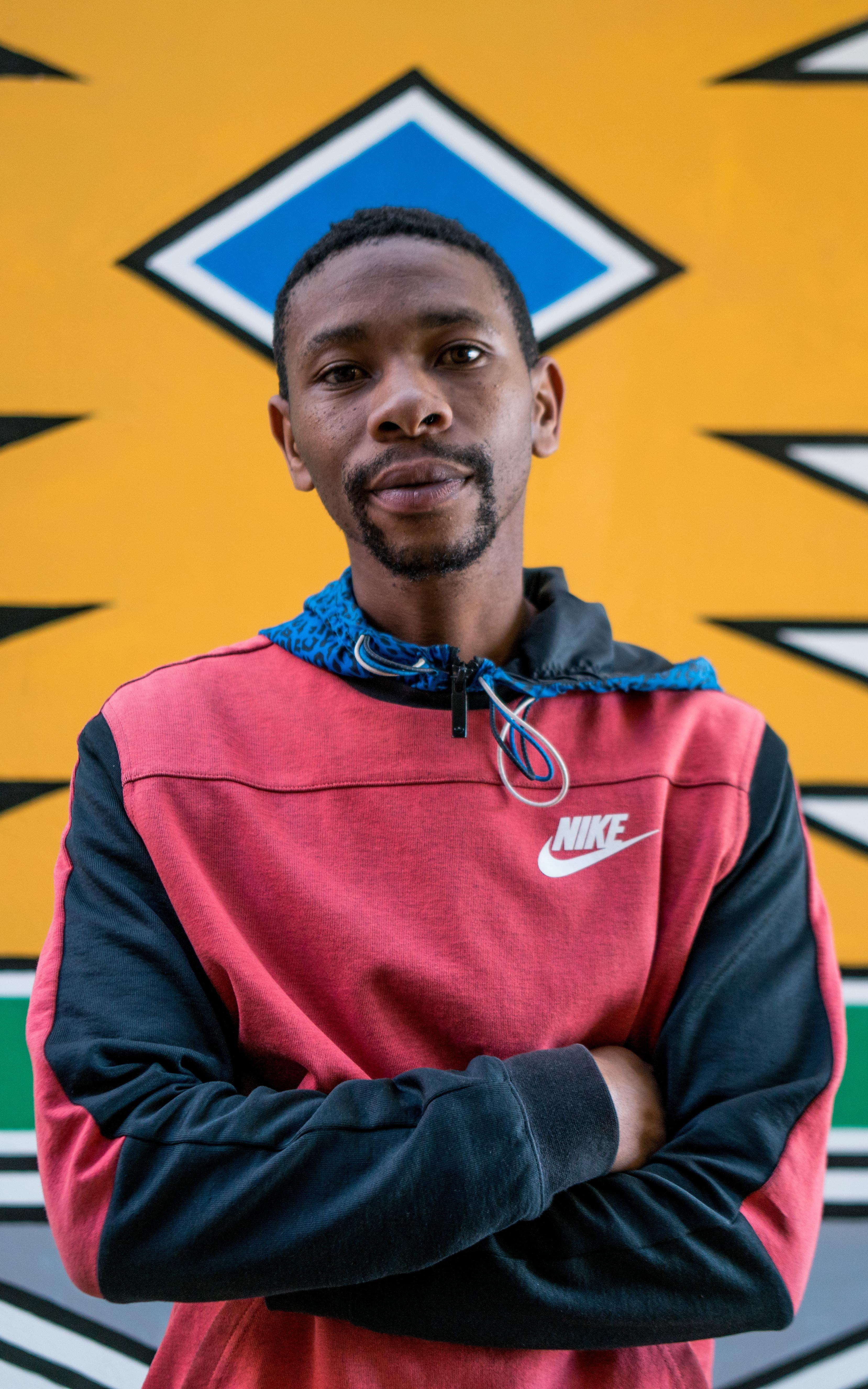 Man stands with his arms crossed in front of a brightly coloured wall