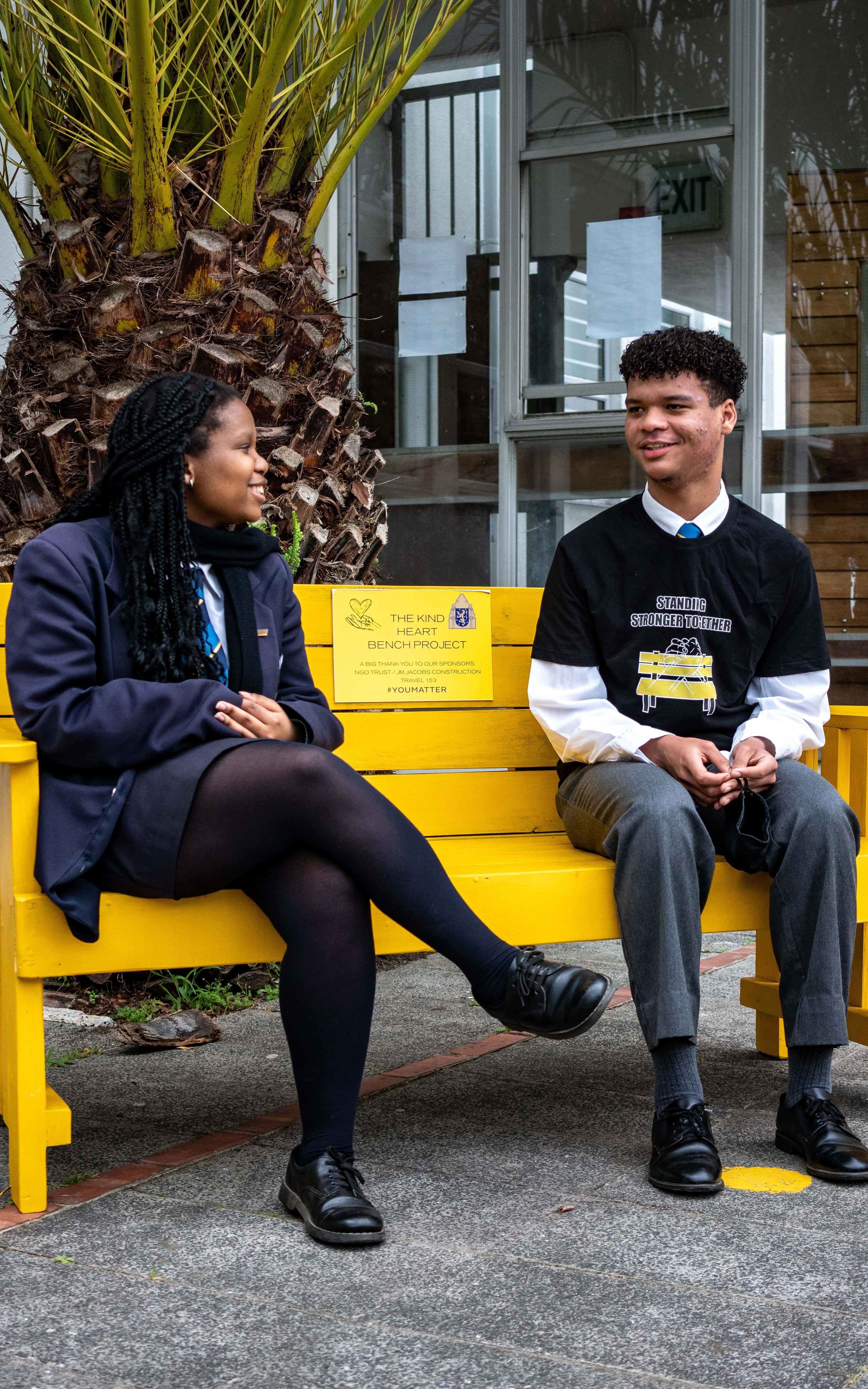 Beautiful News-A high school boy and girl sitting on a yellow bench.