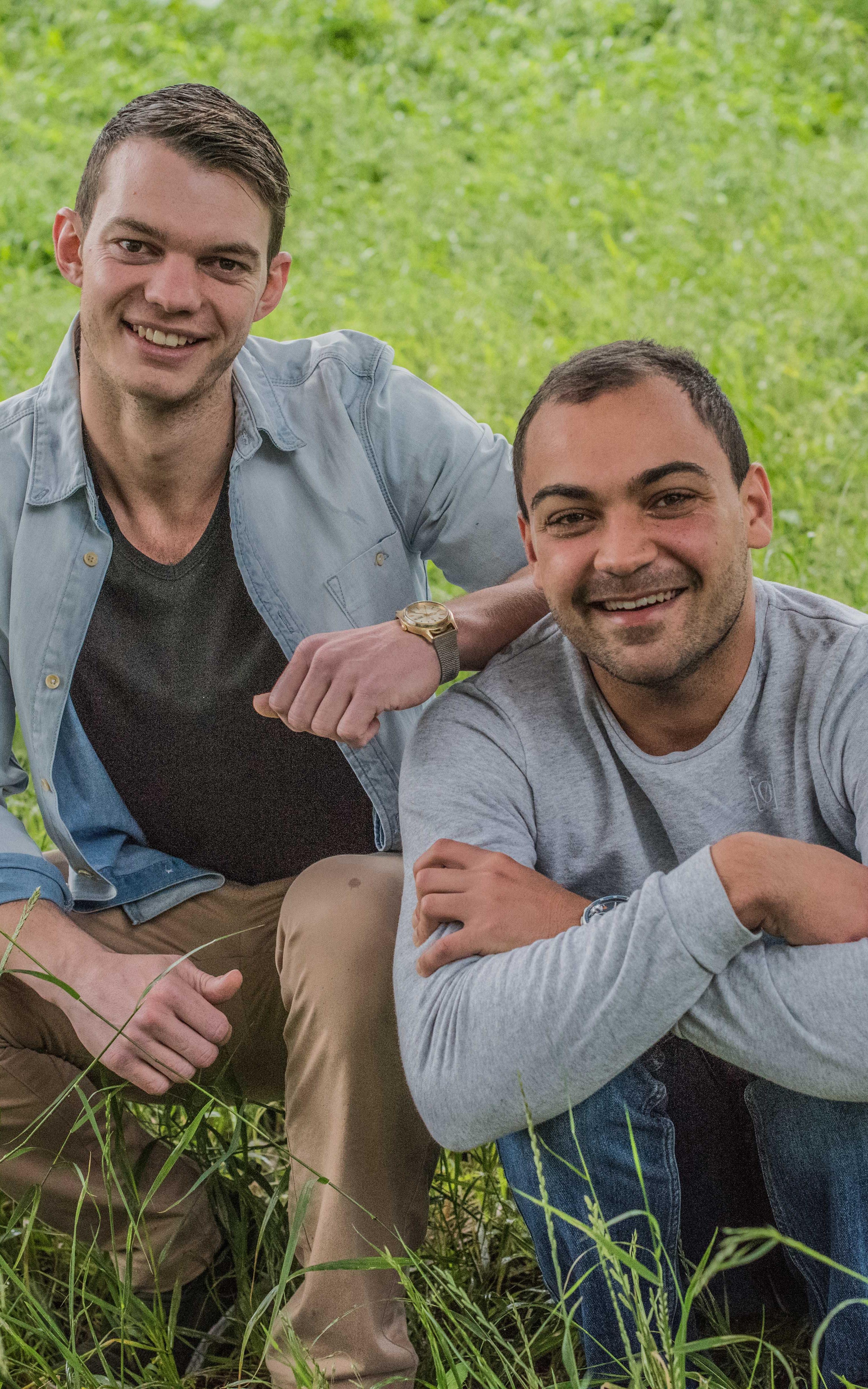 Two men smile in a field of grass