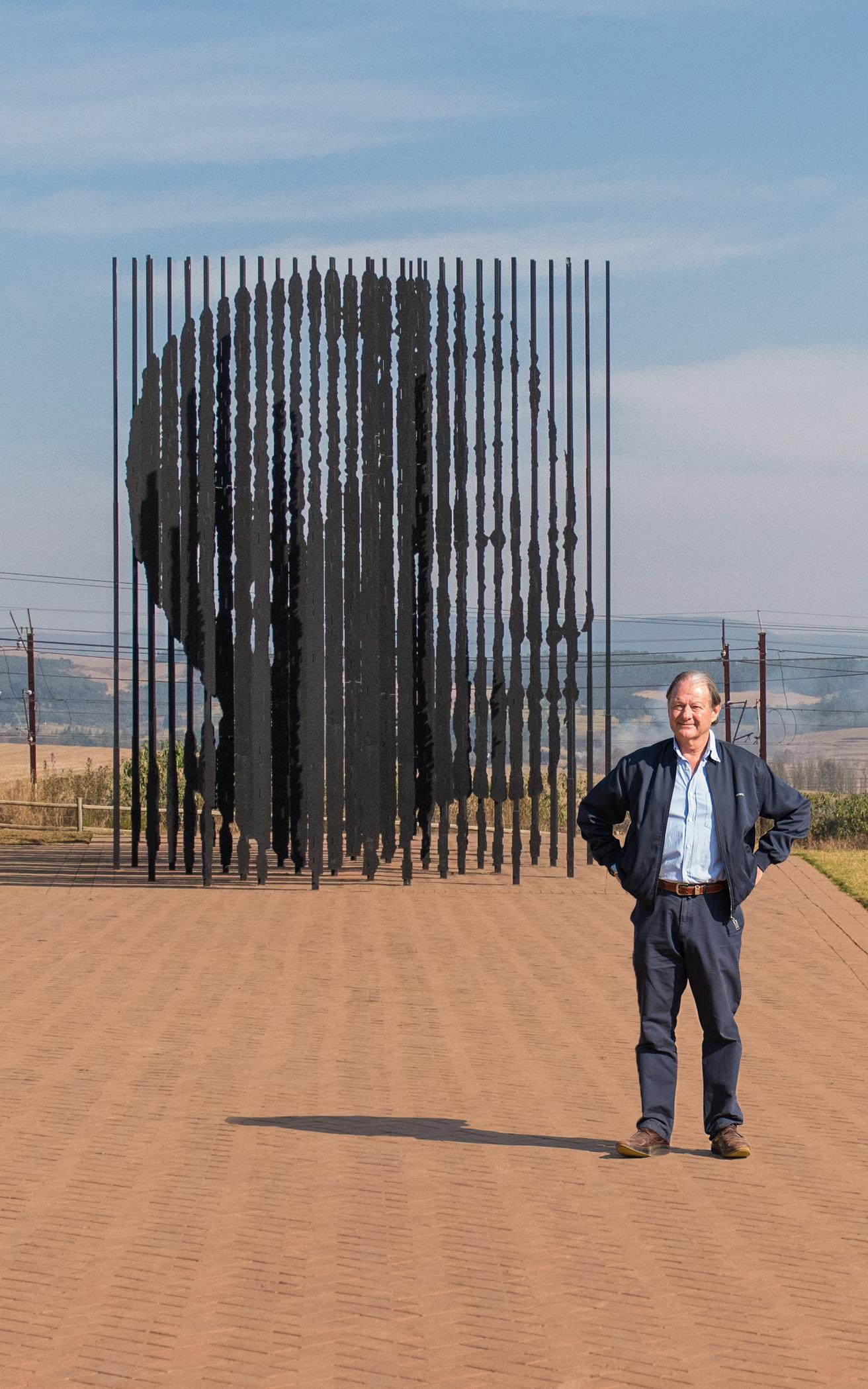 Man stands with his hands on his hips in front of a monument of Nelson Mandela