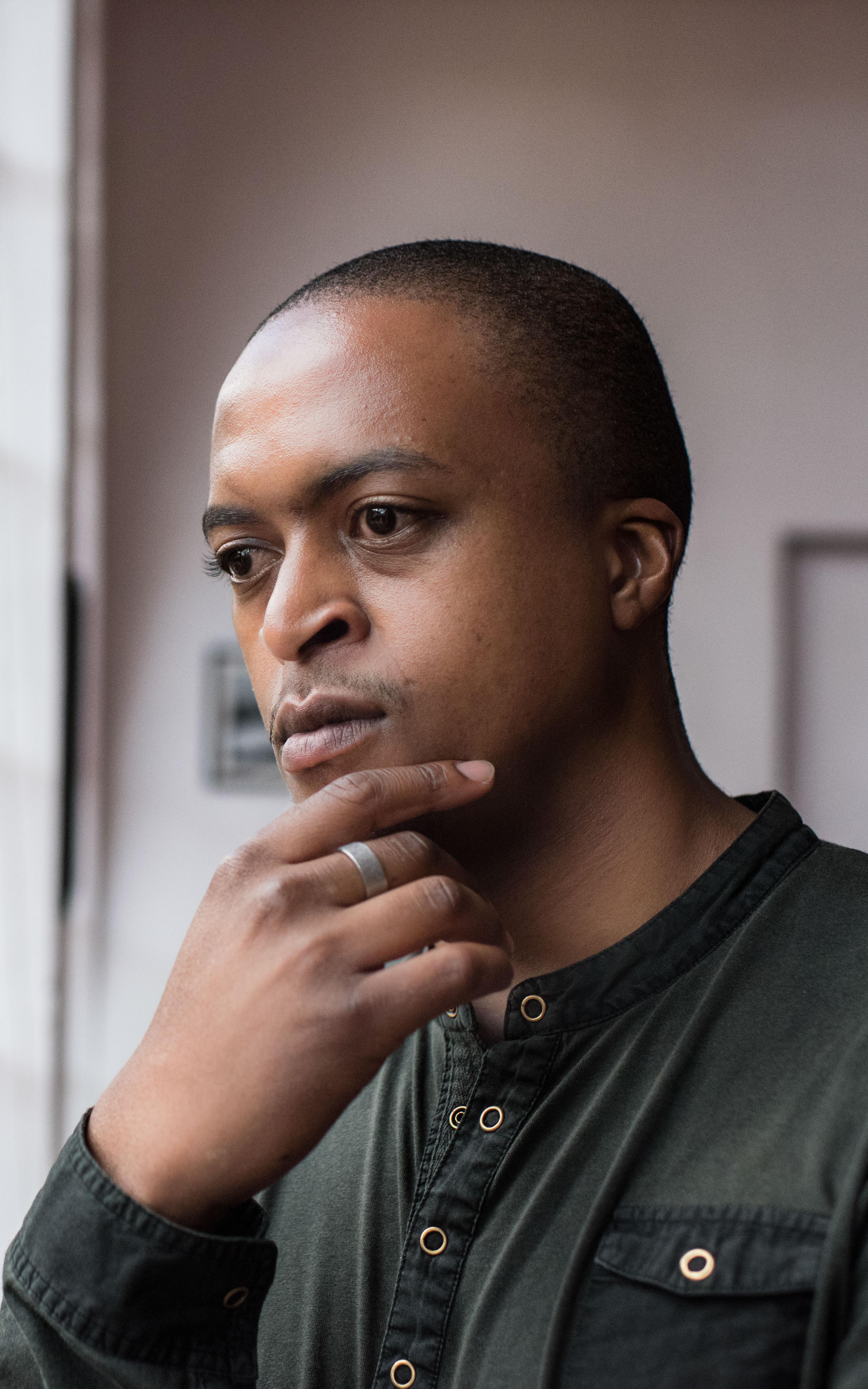 Man looks thoughtfully out a window with his hand on his chin
