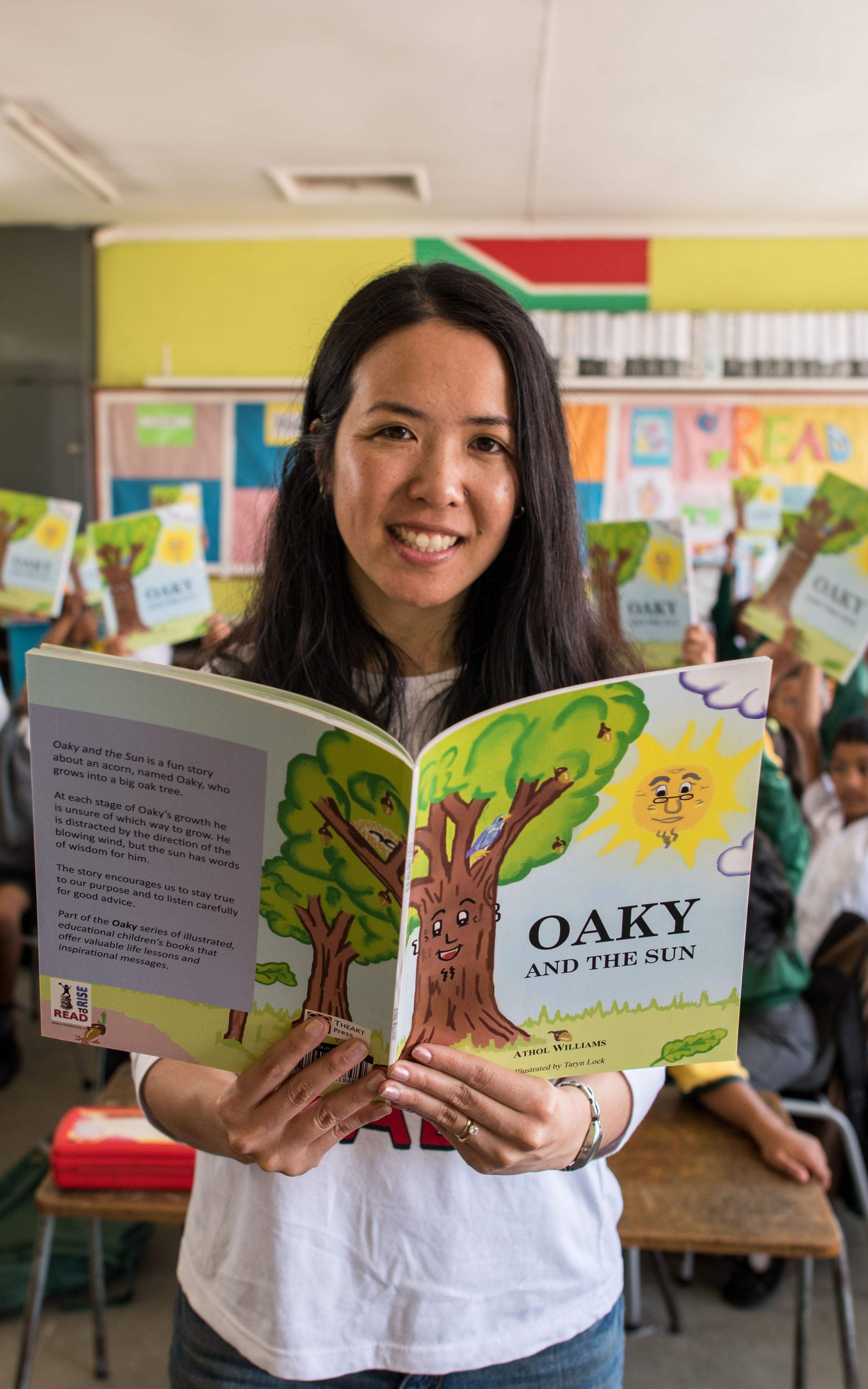 Asian woman with an open reading book in front of a class.