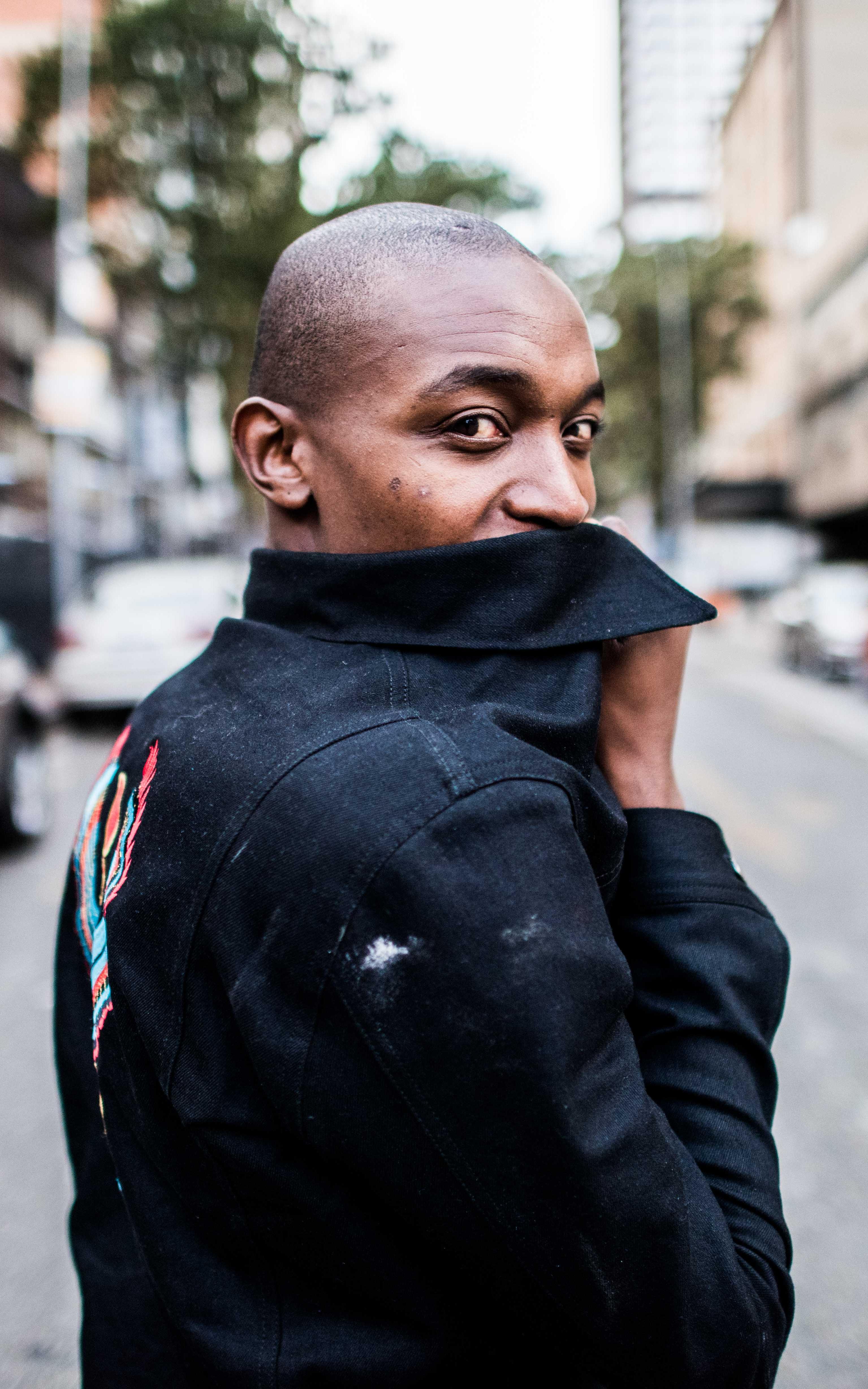 Man looks at the camera while covering his mouth with the collar of a leather jacket