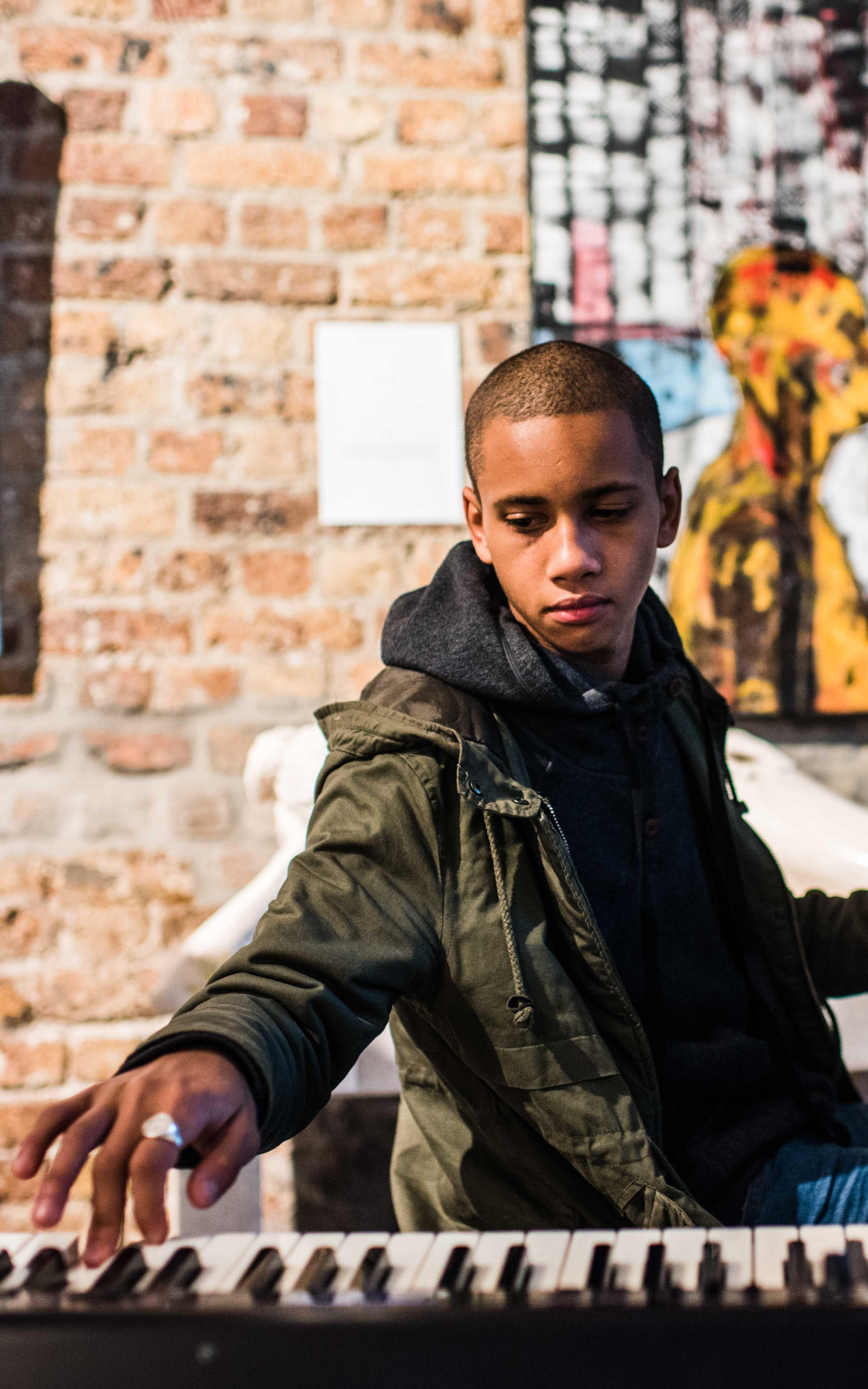 Teenager has one hand on a piano and the other on a keyboard