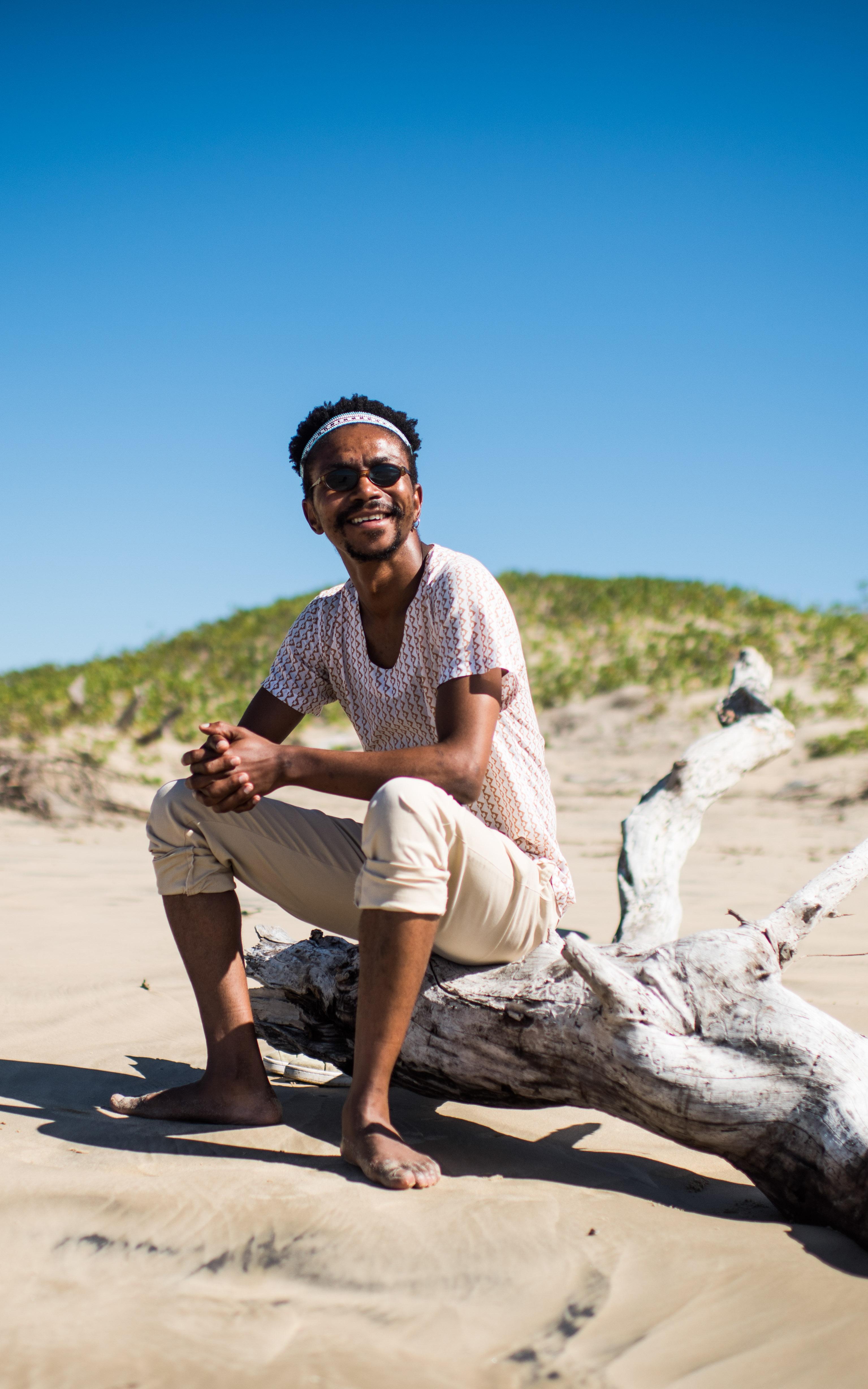 African man sitting on an old tree in the sand