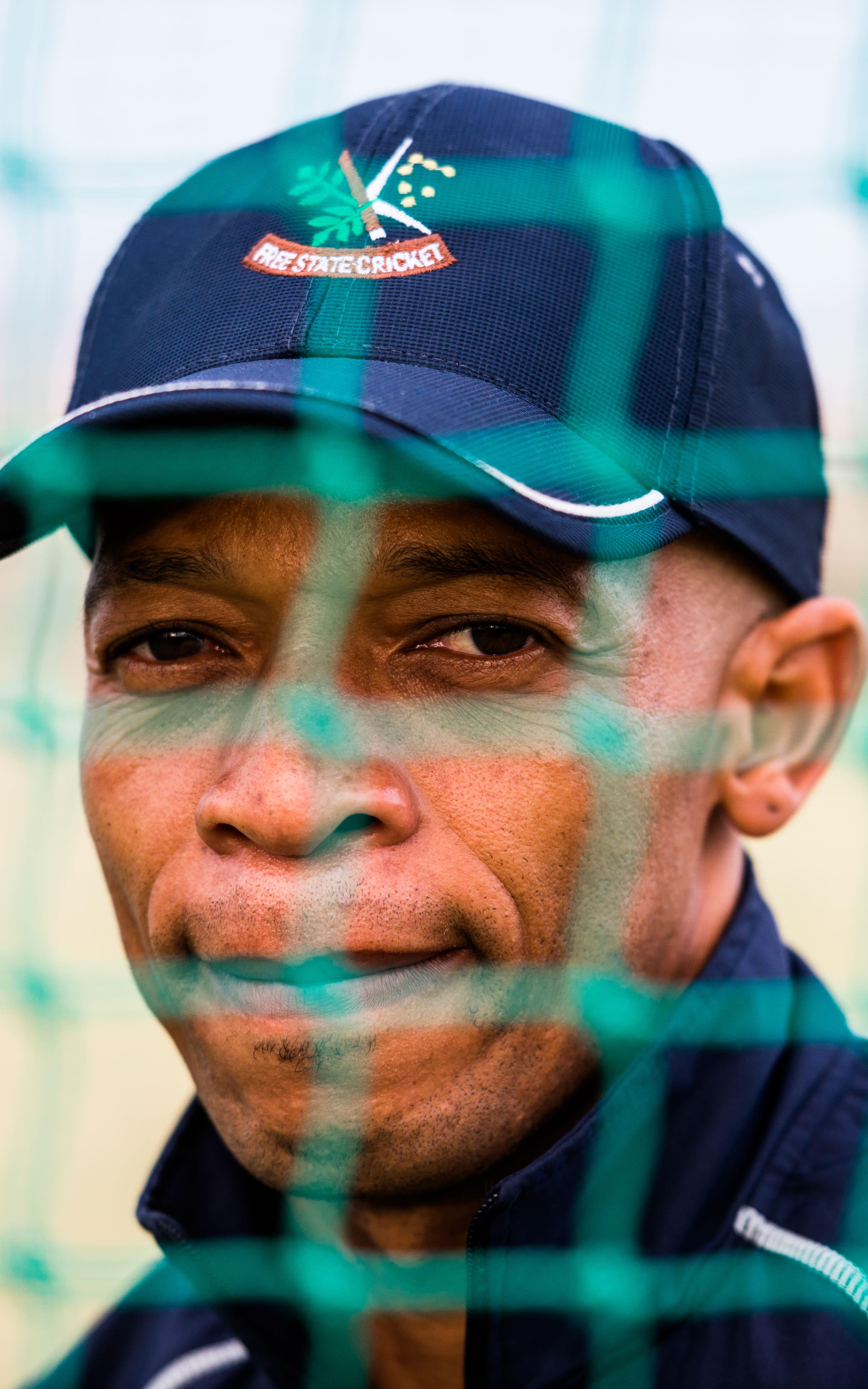 Black cricket coach behind cricket nets.