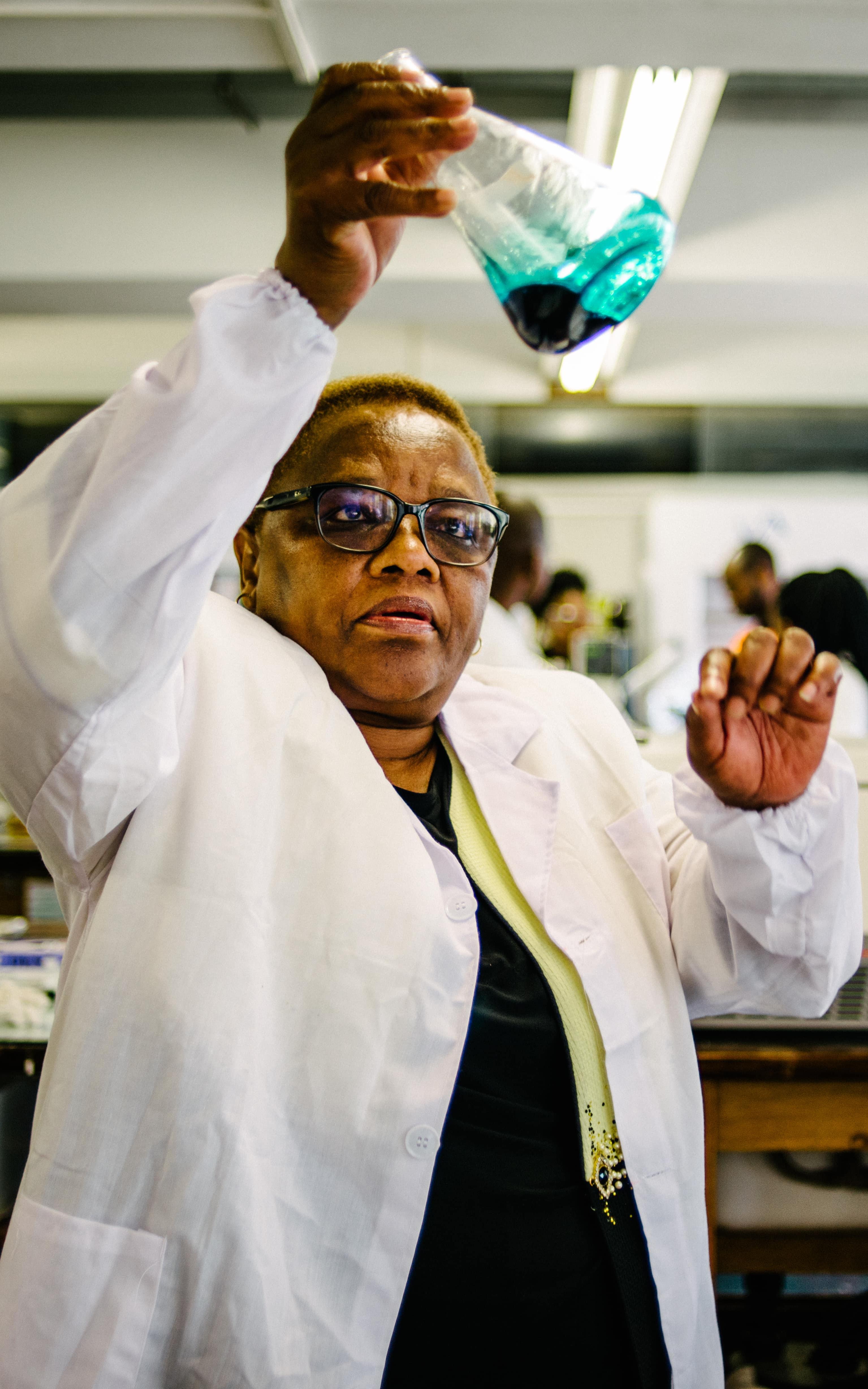 Black woman in a lab holds up a beaker containing liquid
