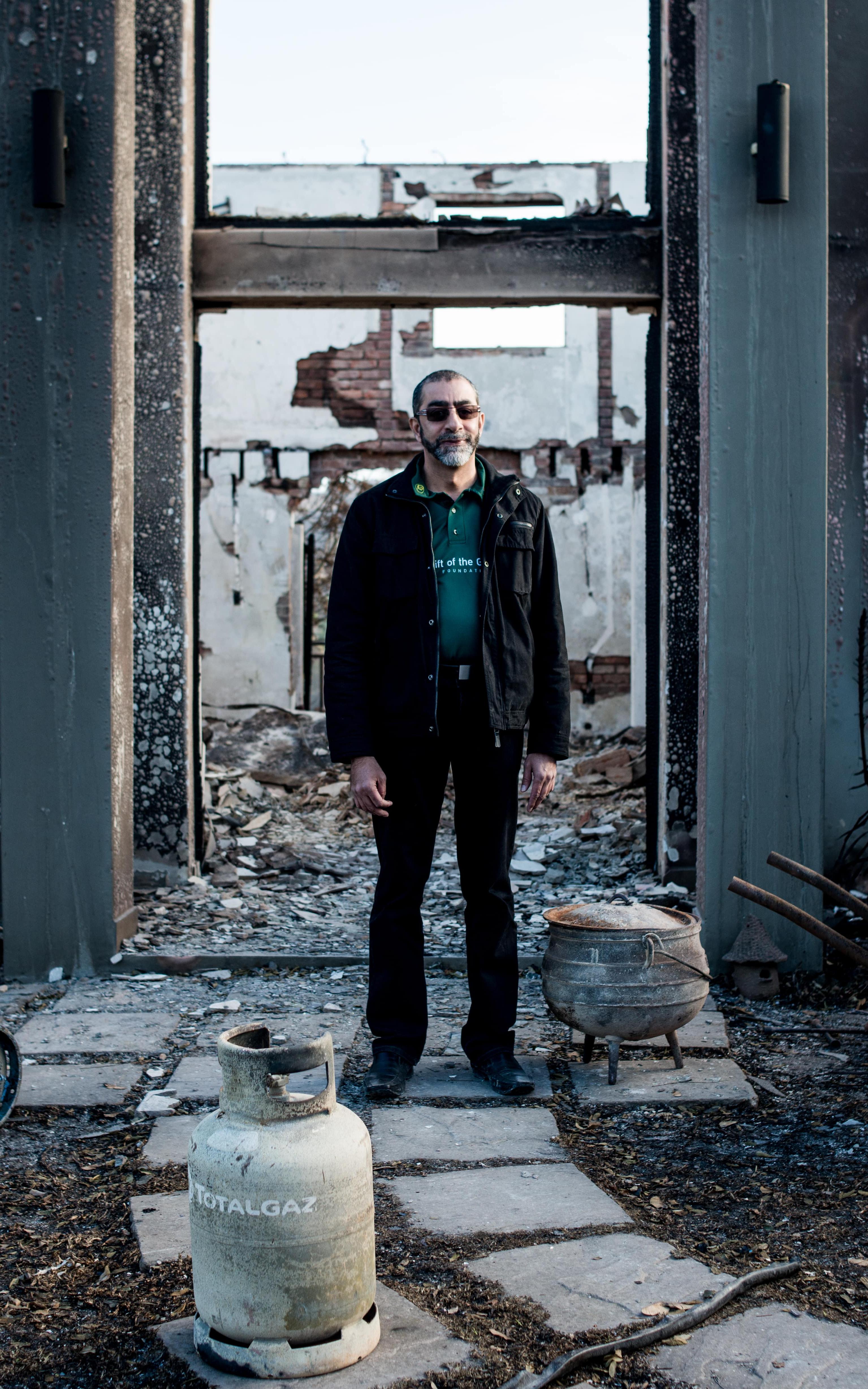 Man stands among the remains of a burned down house