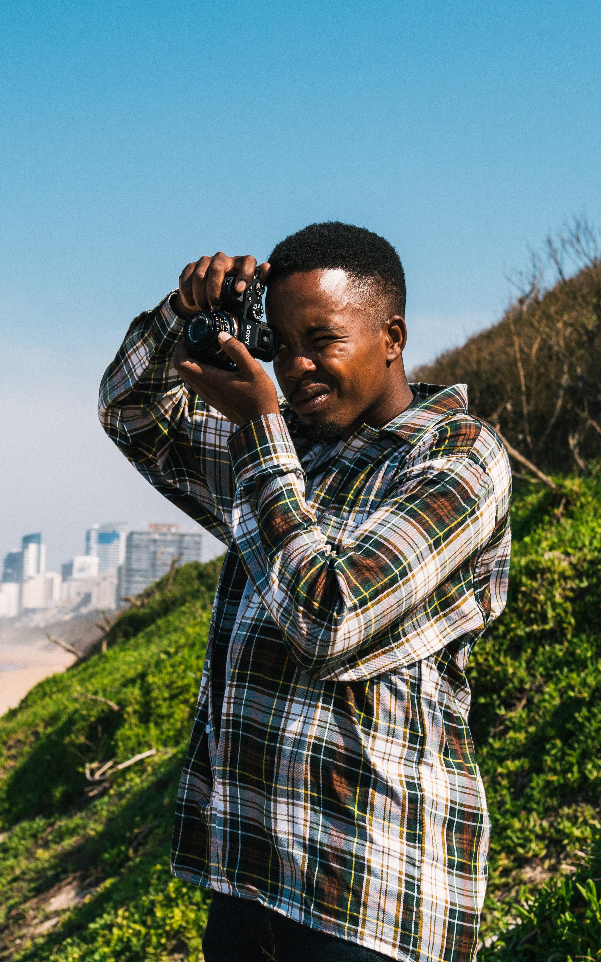 Young man stands on a beach holding a camera up to his eye