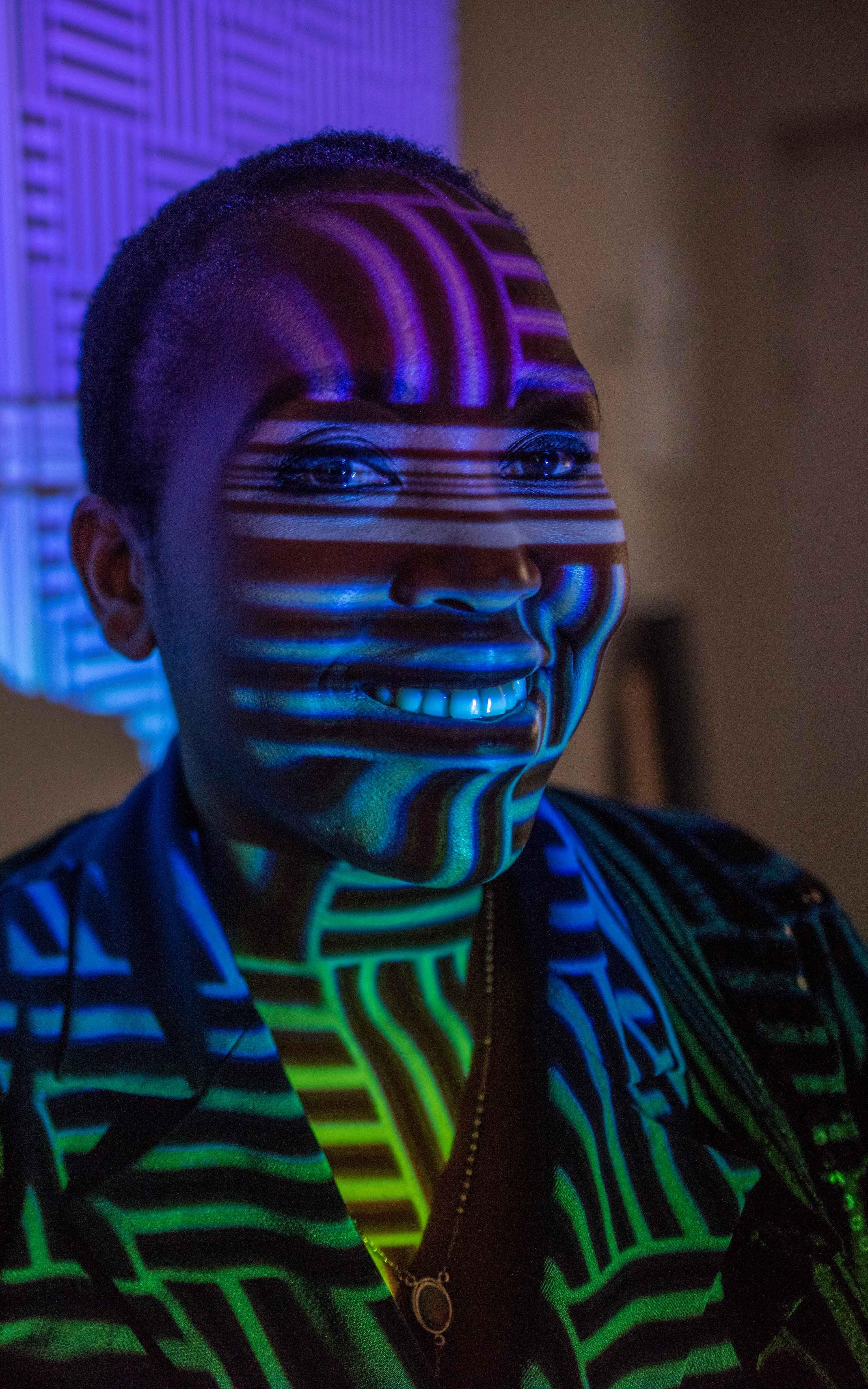 Black woman smiling in front of colourful wall projection.