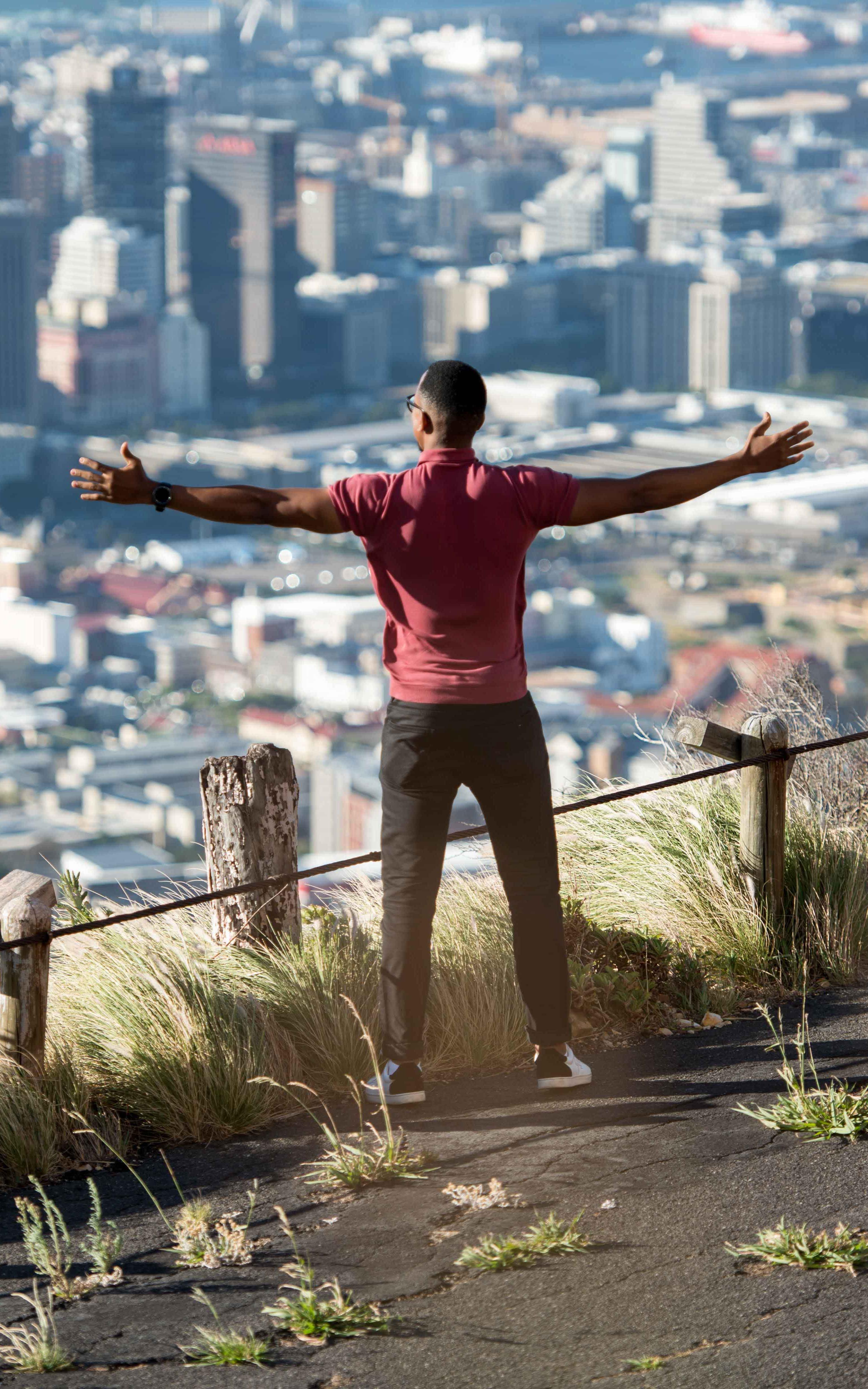 Man stands with his arms outstretched overlooking Cape Town