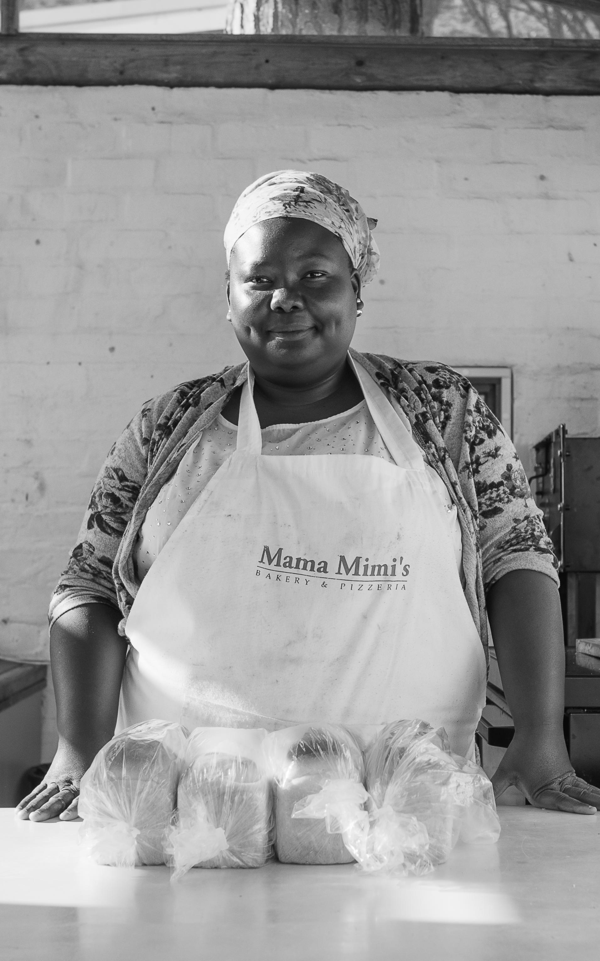 Black lady standing behind a table with bread on it.