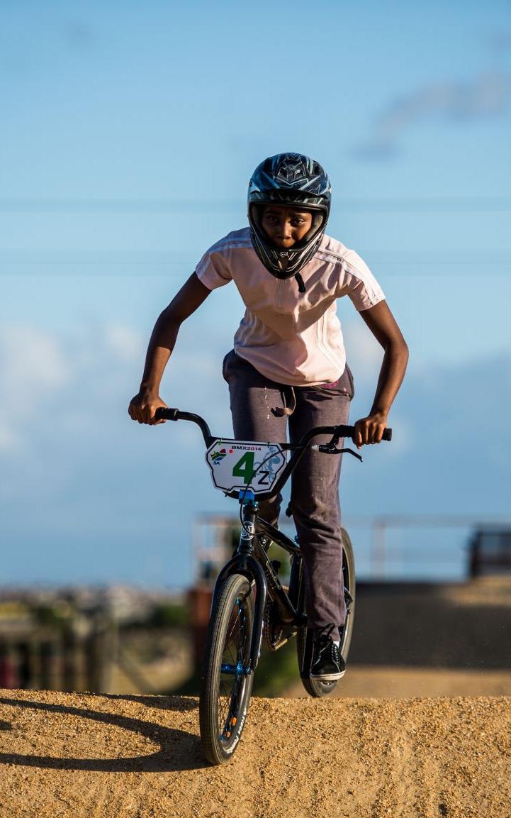 Black girl riding a BMX on dirt track.