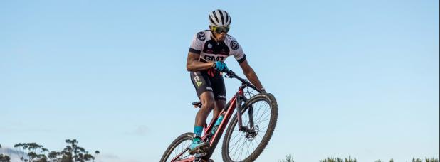 Male cyclist jumping over a dirt ramp.