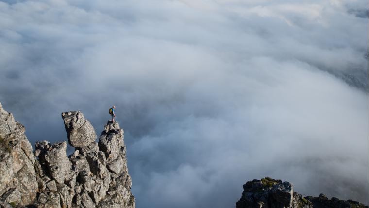 Man stands on the edge of a high mountain surrounded by clouds