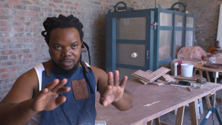 Black ceramicist sitting by his workbench.