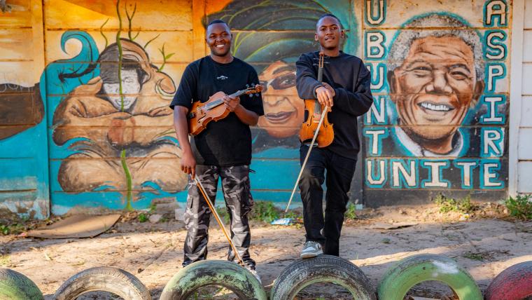 Ayabonga Tshemese, Onke Mbopha, Masi Violin Outreach stand in front of a mural of Nelson Mandela