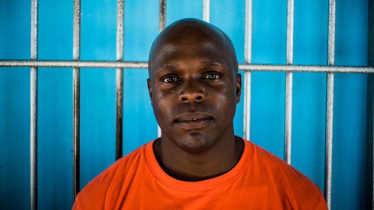 Black man staring into camera in front of blue wall.