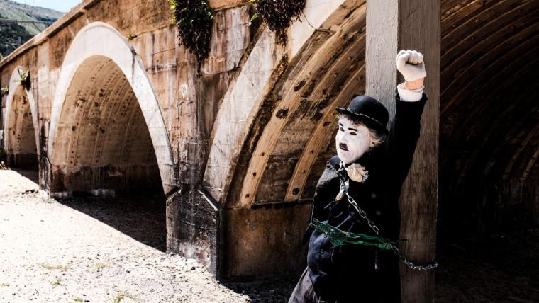 Mime with his fist in the air, tied to a pier support.