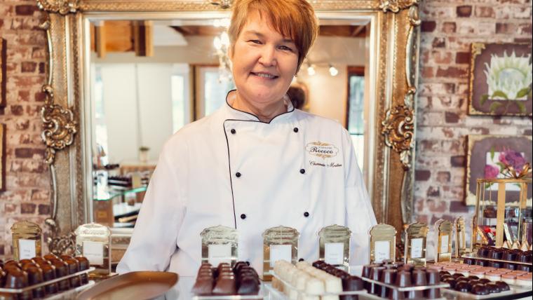 Woman chocolatier behind a counter of chocolates.