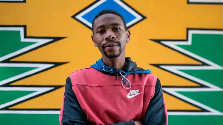 Man stands with his arms crossed in front of a brightly coloured wall