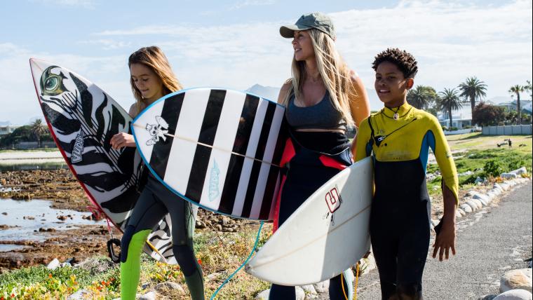 A lady and 2 teenagers with surfboards