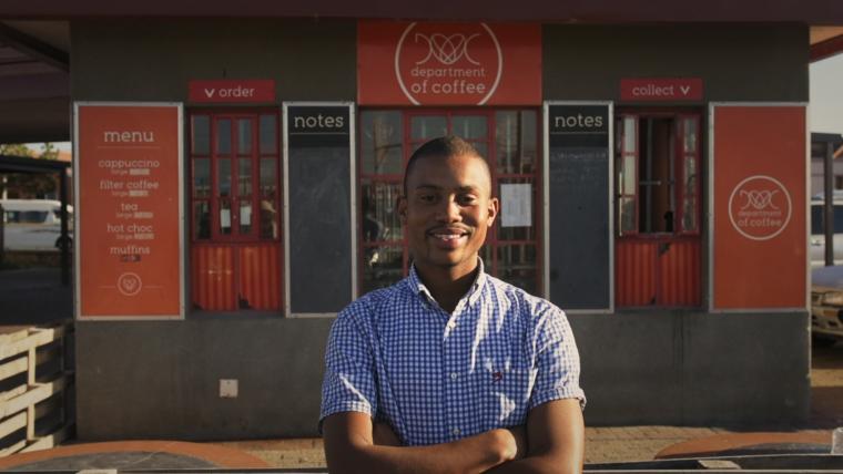 Black coffee business owner in front of his store.