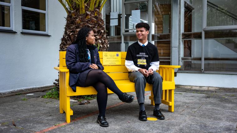 Beautiful News-A high school boy and girl sitting on a yellow bench.