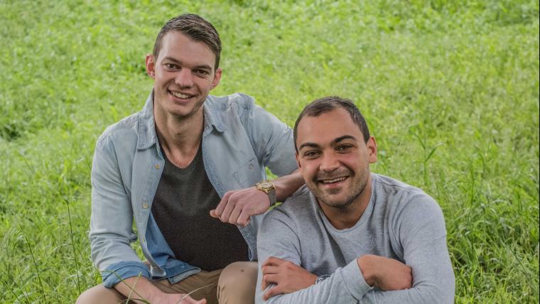 Two men smile in a field of grass
