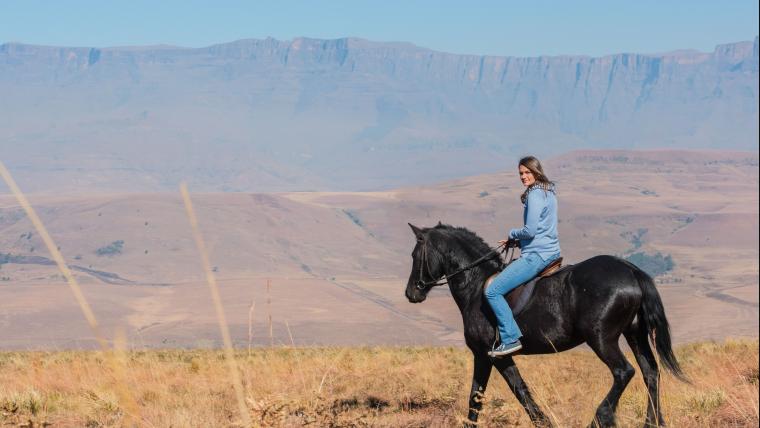 Woman rides a horse with mountains in the background