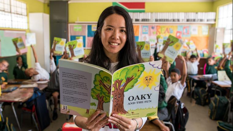 Asian woman with an open reading book in front of a class.