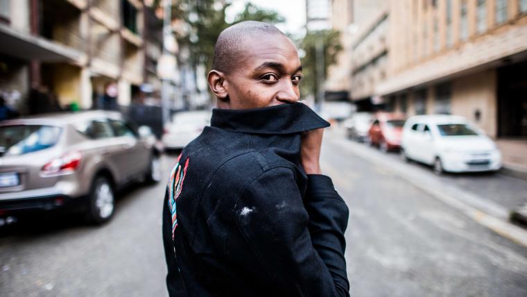 Man looks at the camera while covering his mouth with the collar of a leather jacket