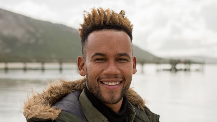 Man smiles at the camera standing in front of a lagoon