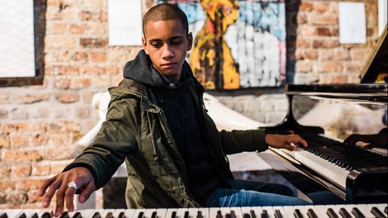 Teenager has one hand on a piano and the other on a keyboard