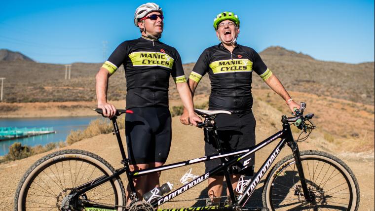 Two men standing by tandem bicycle