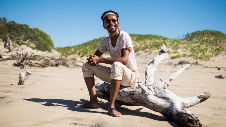 African man sitting on an old tree in the sand