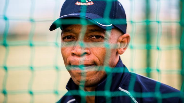 Black cricket coach behind cricket nets.