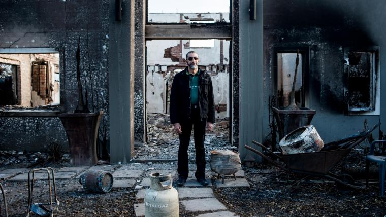 Man stands among the remains of a burned down house