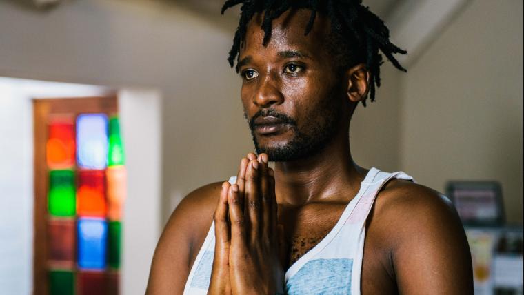 Man stands in a yoga position with his palms pressed together