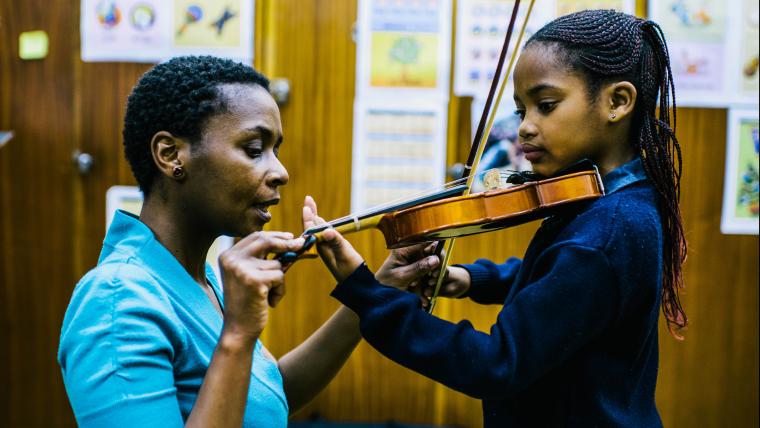 Woman showing girl how to play violin