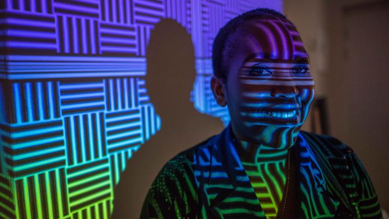 Black woman smiling in front of colourful wall projection.