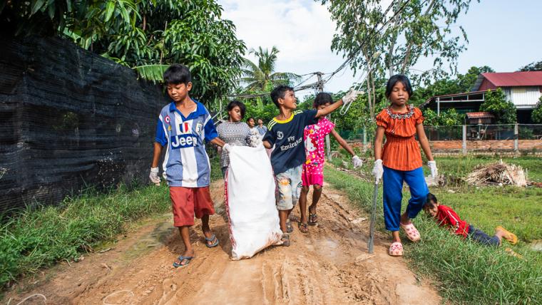 Beautiful News - Children in Cambodia walking along a sand road collecting litter