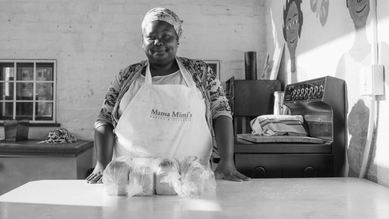 Black lady standing behind a table with bread on it.