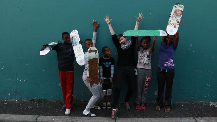 Woman with group of kids holding skareboards.