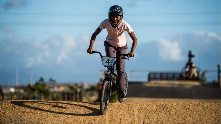 Black girl riding a BMX on dirt track.