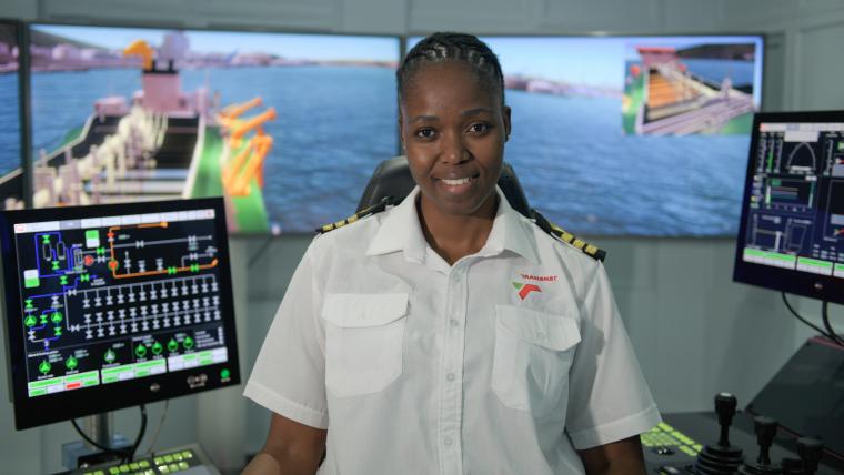 Woman smiles wearing a sailing uniform in front of sailing equipment